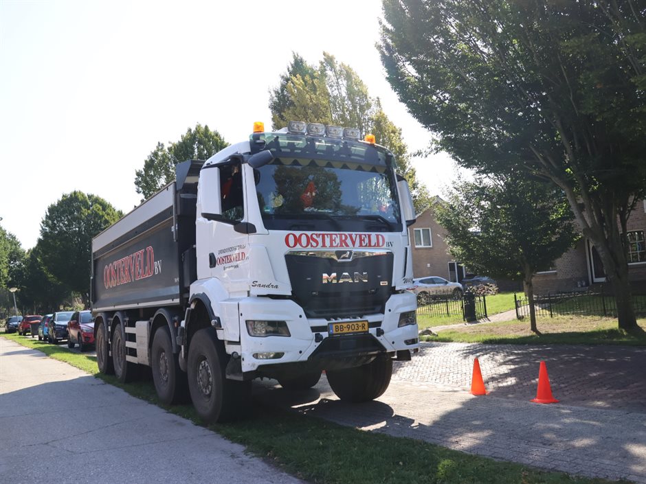 Vrachtwagen van Oosterveld staat geparkeerd bij een school, met pionnen op de stoep.